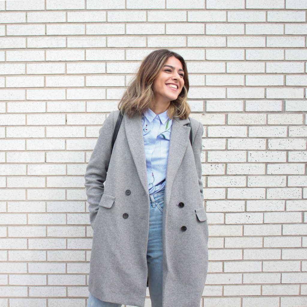 femme portant un jean un chemisier bleu et un manteau gris